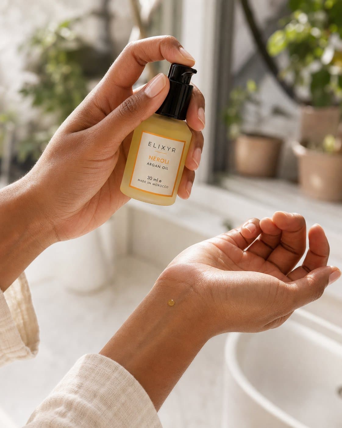 A hand warming a single drop of ELIXYR argan oil