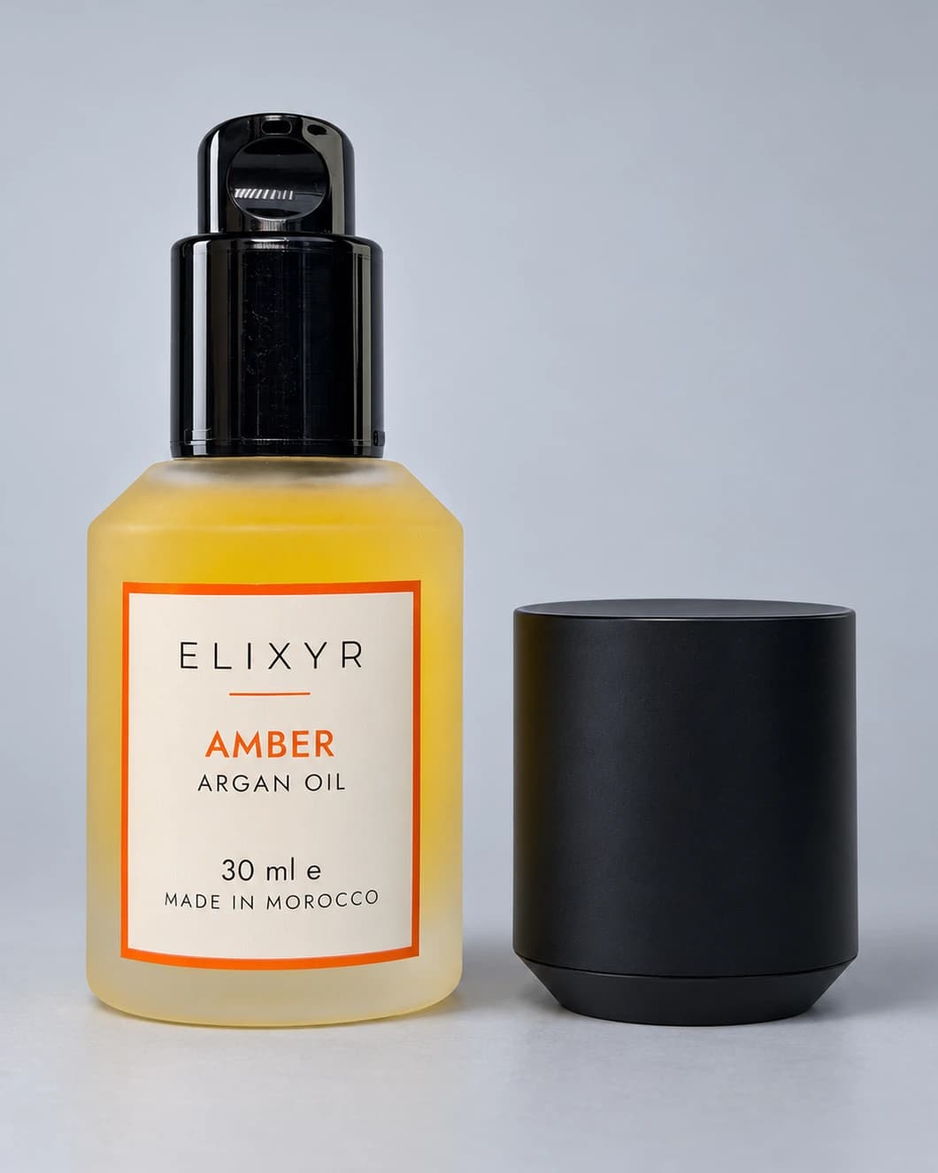 ELIXYR Amber 30ml fragranced argan oil in frosted glass, glossy black pump exposed with the matte black cap beside it