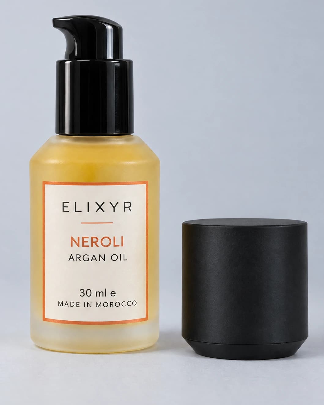 ELIXYR Neroli 30ml fragranced argan oil in frosted glass, glossy black pump exposed with the matte black cap beside it